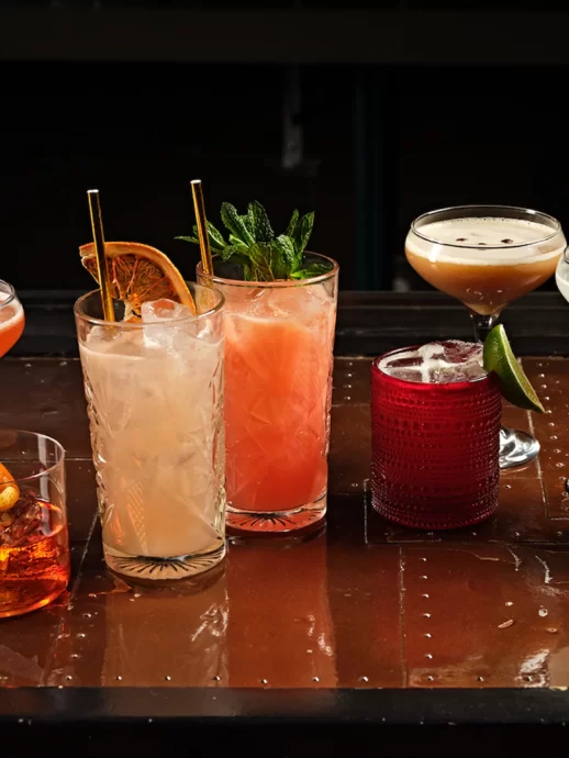 Assorted colorful cocktails in various glasses arranged on a polished bar surface.