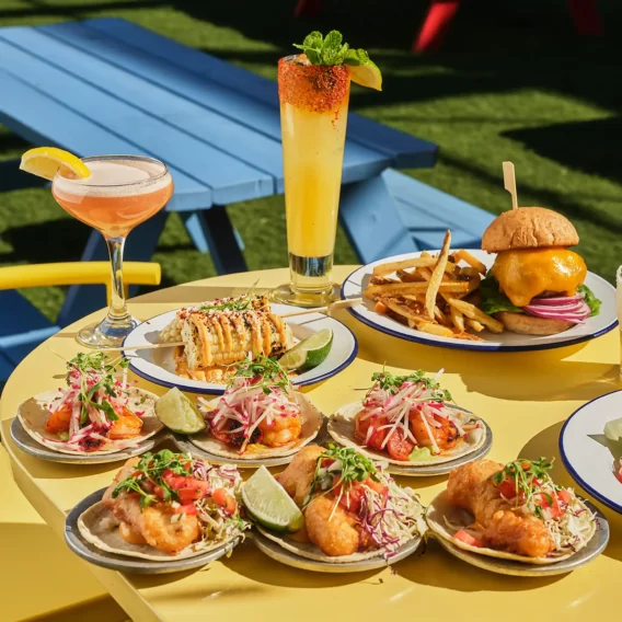 Outdoor dining with tacos, cocktails, fries, and a burger on a sunny day.